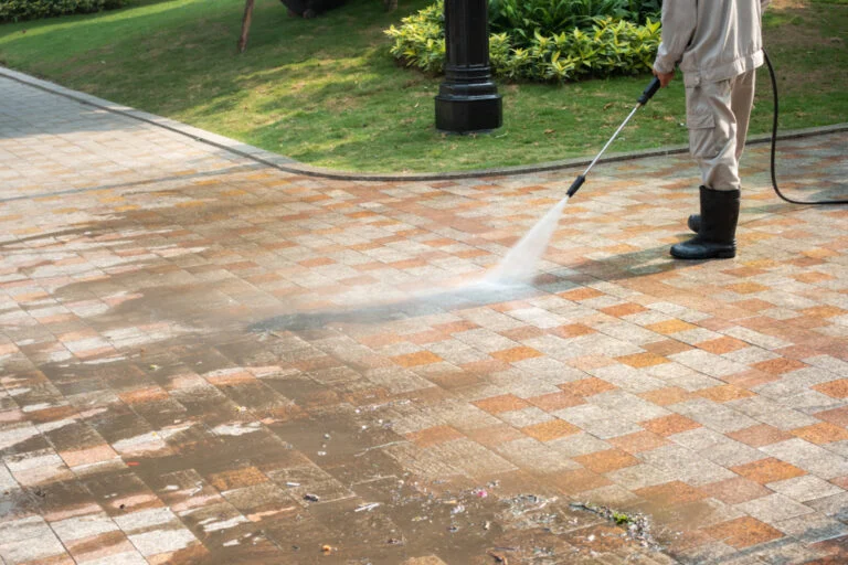 Worker pressure washing an exterior paved area