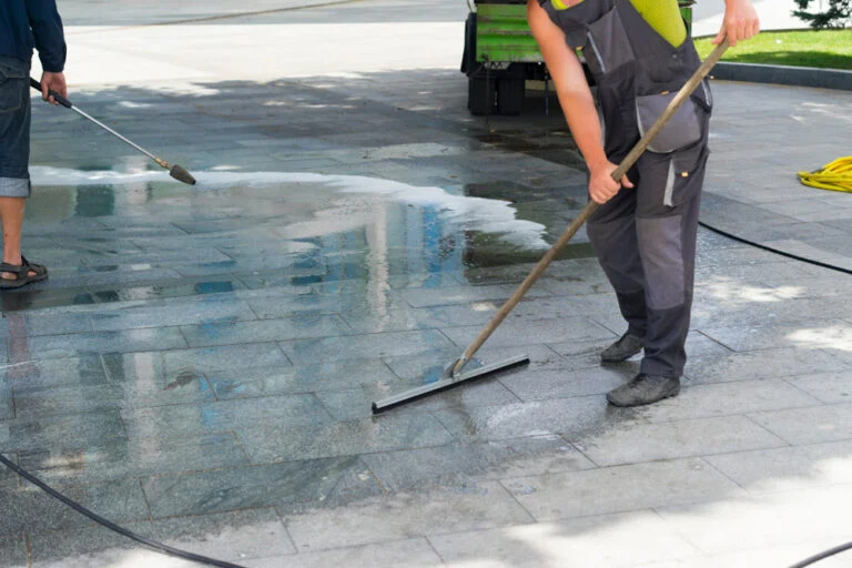 Worker pressure washing an exterior paved area