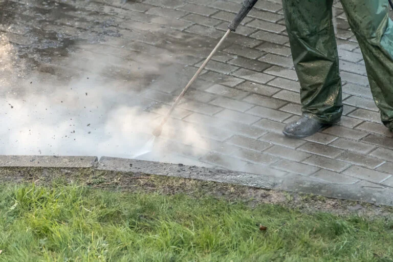 Worker pressure washing an exterior paved area