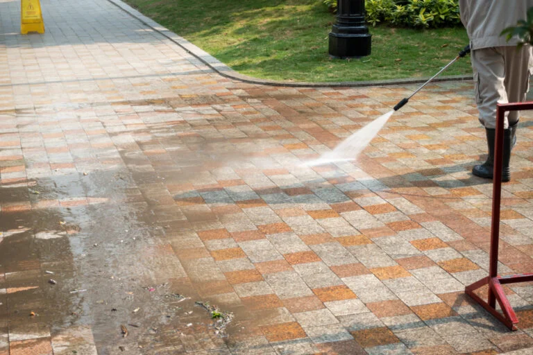 Worker pressure washing an exterior paved area
