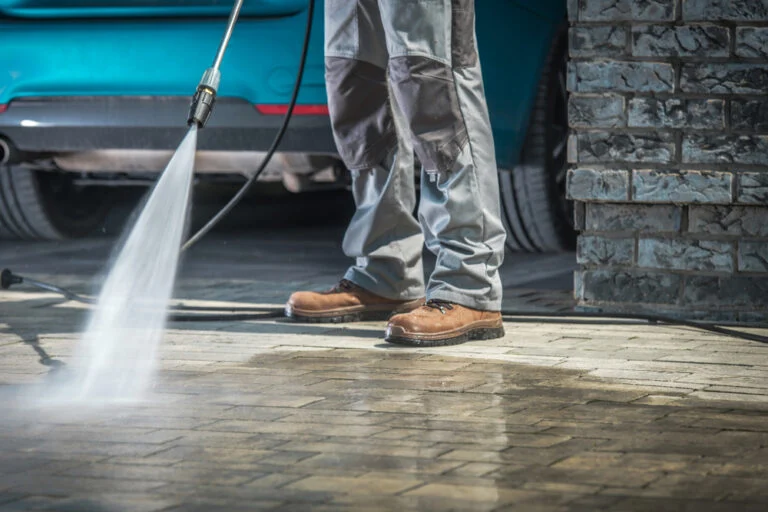 Worker pressure washing an exterior paved area