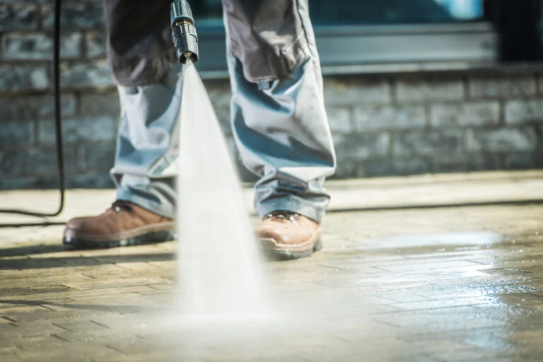 Worker pressure washing an exterior paved area