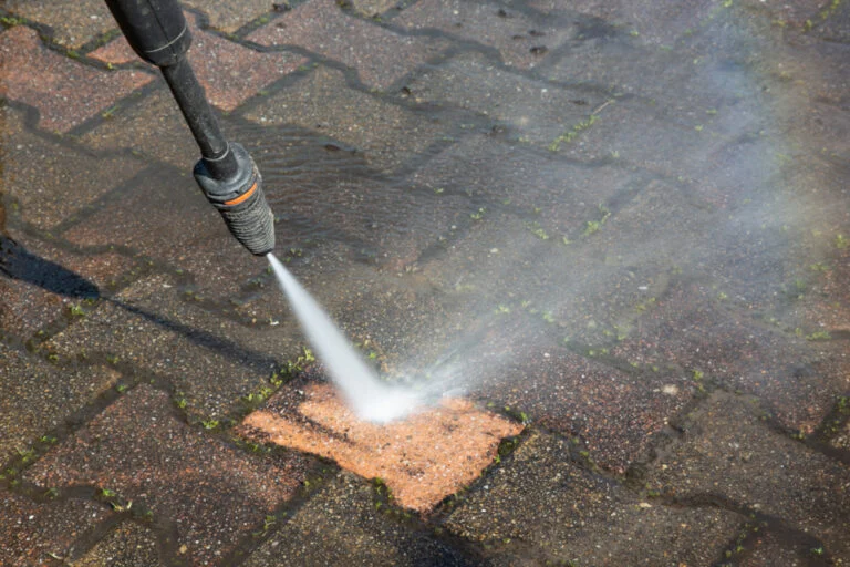 Worker pressure washing an exterior paved area