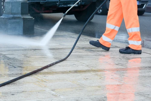 Worker pressure washing an exterior paved area