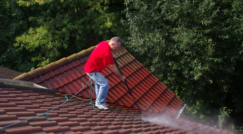 Worker washing a red tiled roof