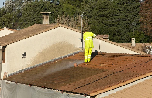 Worker cleaning a flat roof beside a parapet wall
