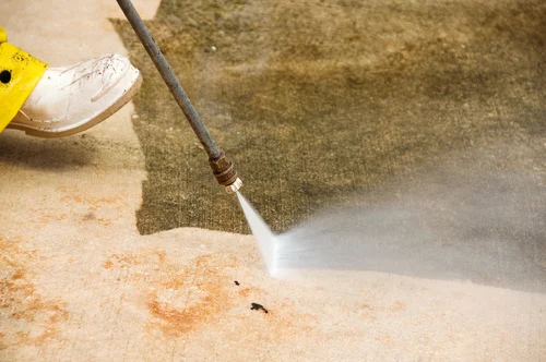 Worker pressure washing an exterior paved area