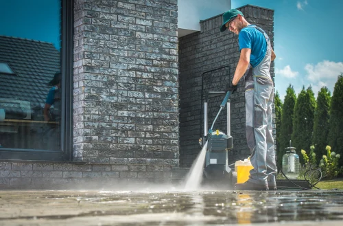 Worker pressure washing an exterior paved area