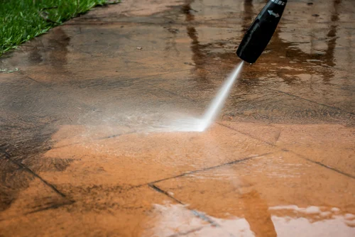 Worker pressure washing an exterior paved area