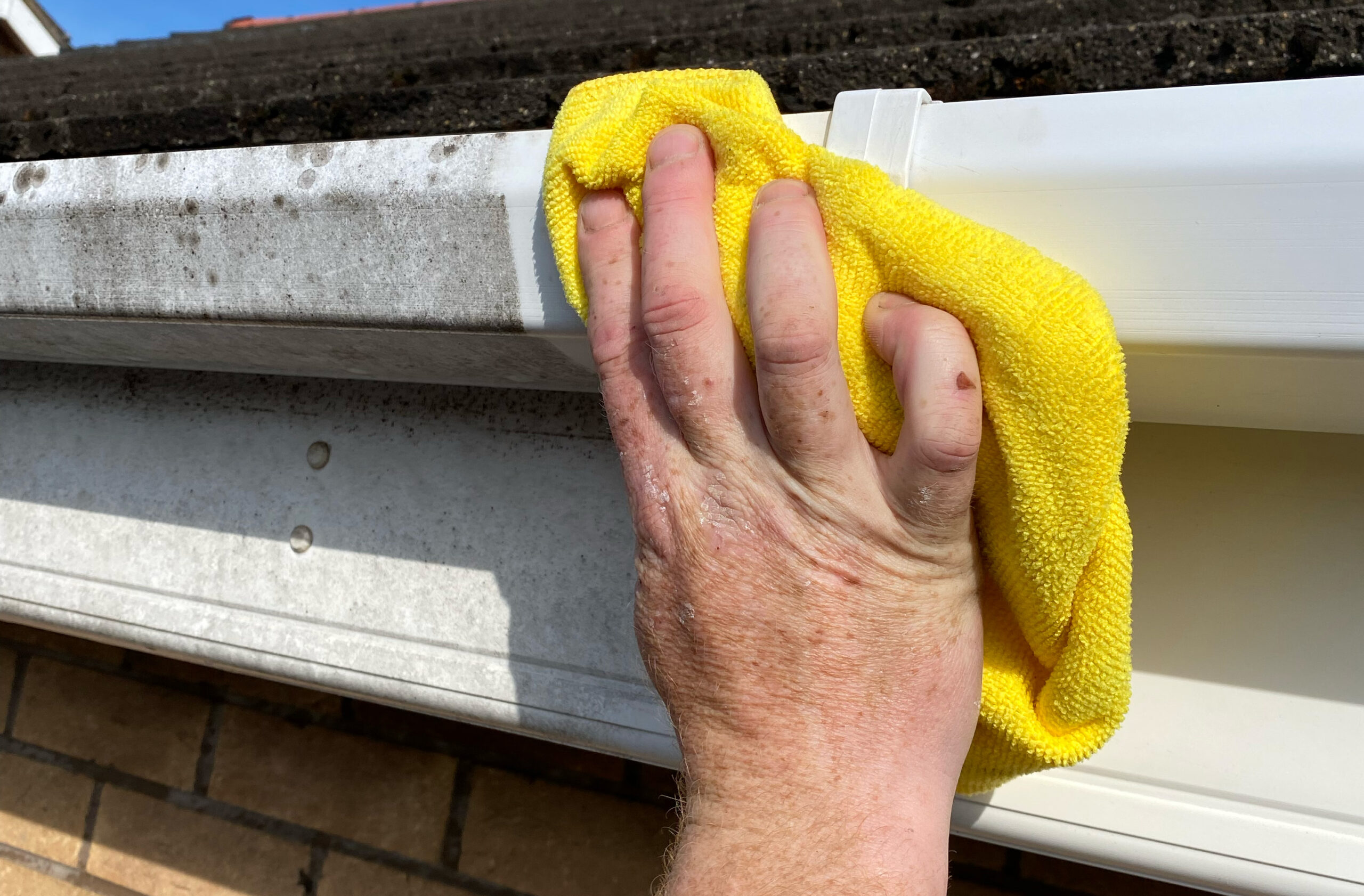 Man cleaning gutter fascia with yellow cloth
