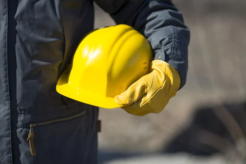 Worker wearing gloves and holding a hard hat