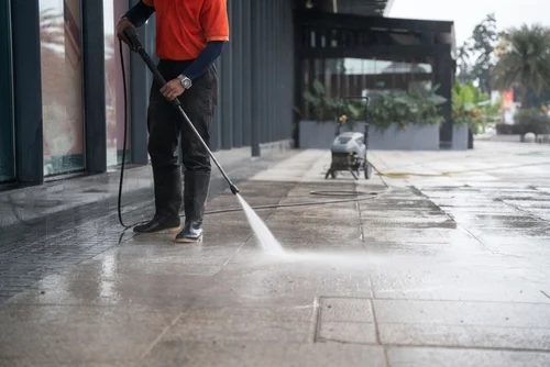 Worker pressure washing an exterior paved area